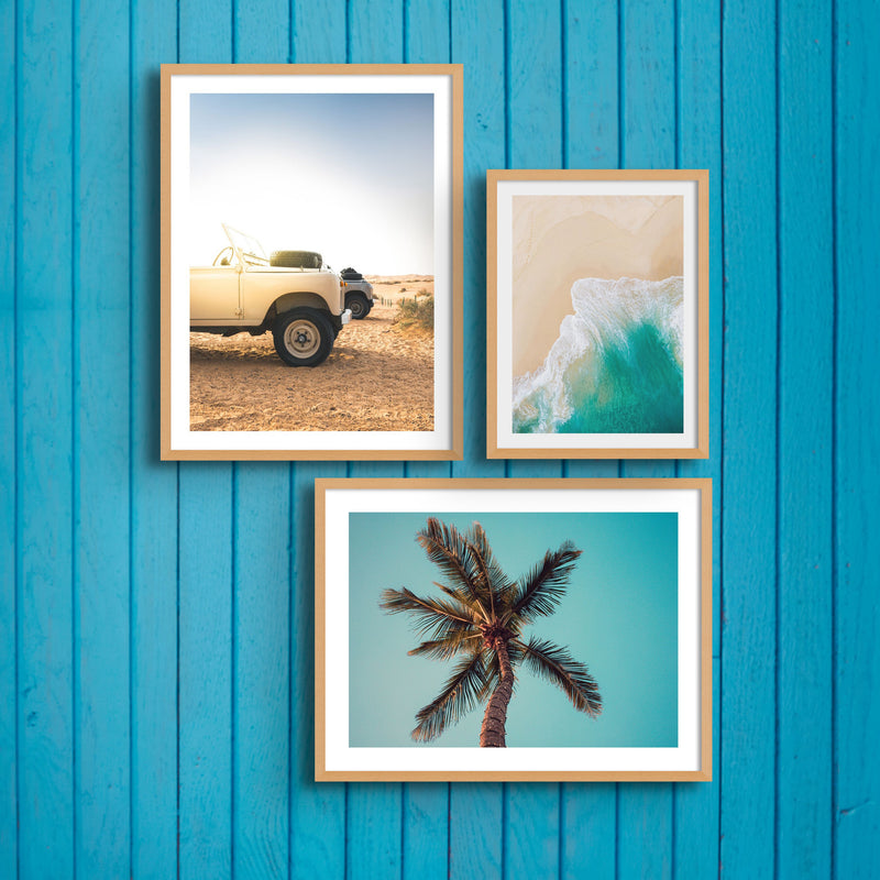 three coastal photographs in natural frames on a weathered blue panelled wall.