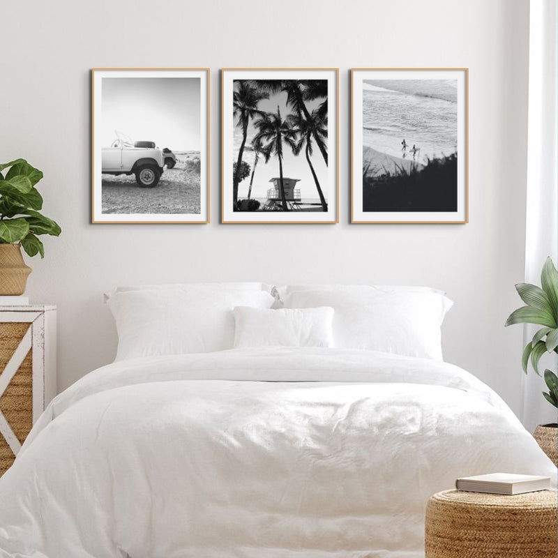 Three black and white photogrpahs of coastal themes in natural frames above a white bed in a coastal bedroom