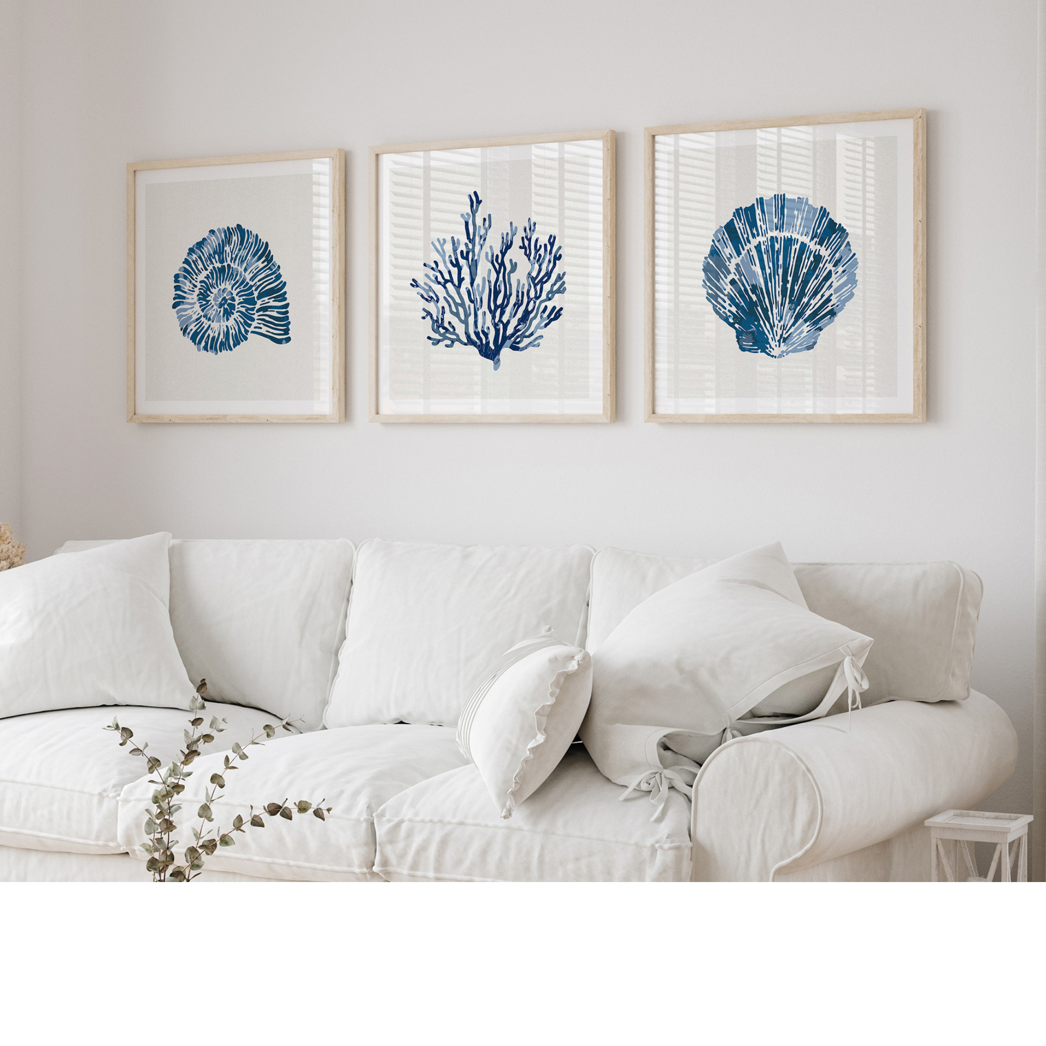 Set of three coastal shell prints above a white sofa in a beachy living room