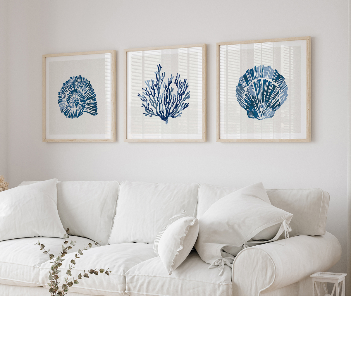 Set of three coastal shell prints above a white sofa in a beachy living room