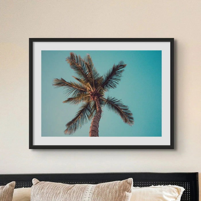 coloured beach art photograph of a palm tree against a blue green sky in a black frame in a neutral coastal bedroom- beach house art